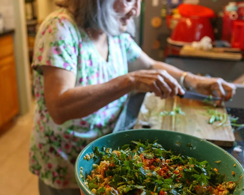 Mujer picando cilantro junto a un tazón de ensalada fresca en su cocina