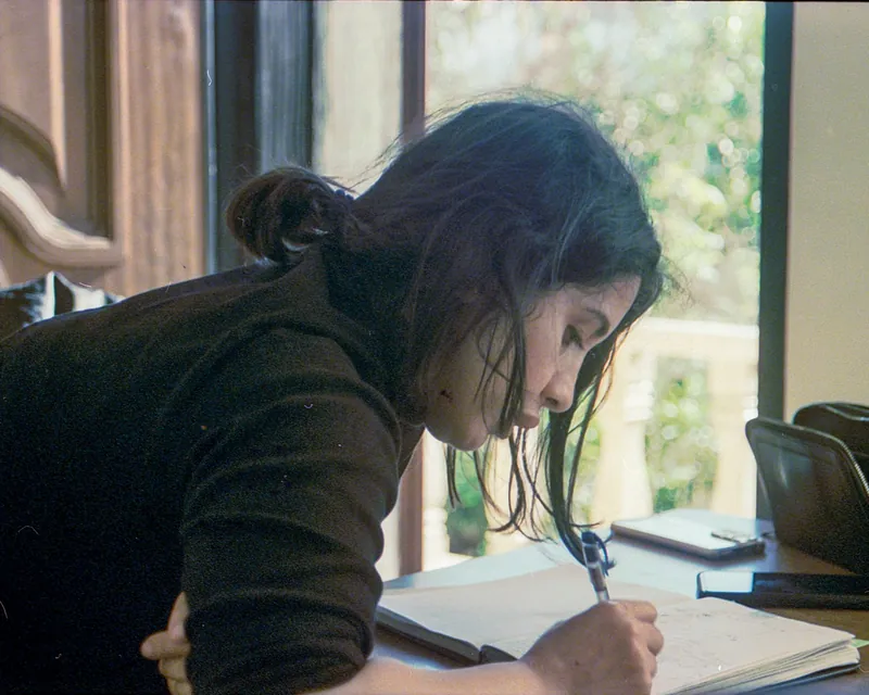 Mujer escribiendo en su cuaderno junto a una ventana