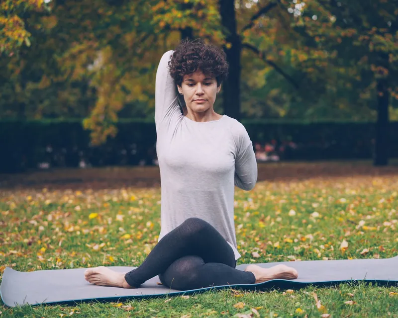 Mujer estirando sobre un tapete de yoga en un parque en otoño